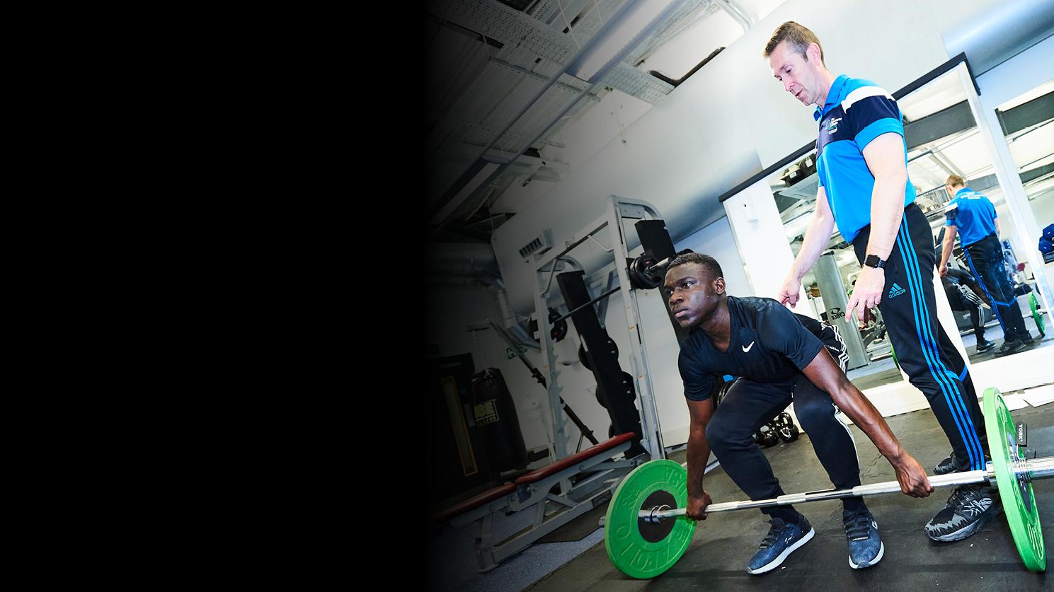 A personal trainer supervising a young man lifting weights at the gym