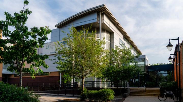 Exterior view of the UCEN Manchester Nicholls campus building surrounded by trees and landscaped walkways.