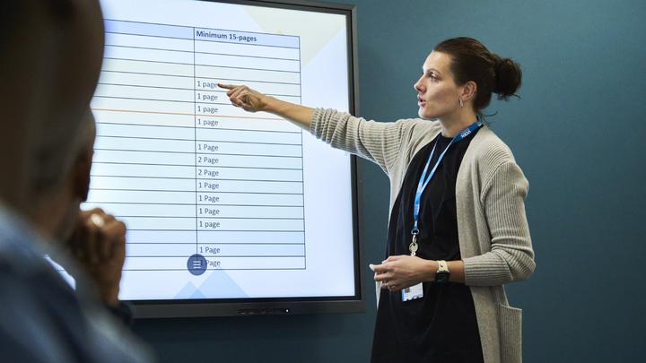 Business tutor in front of a class pointing at a smarboard