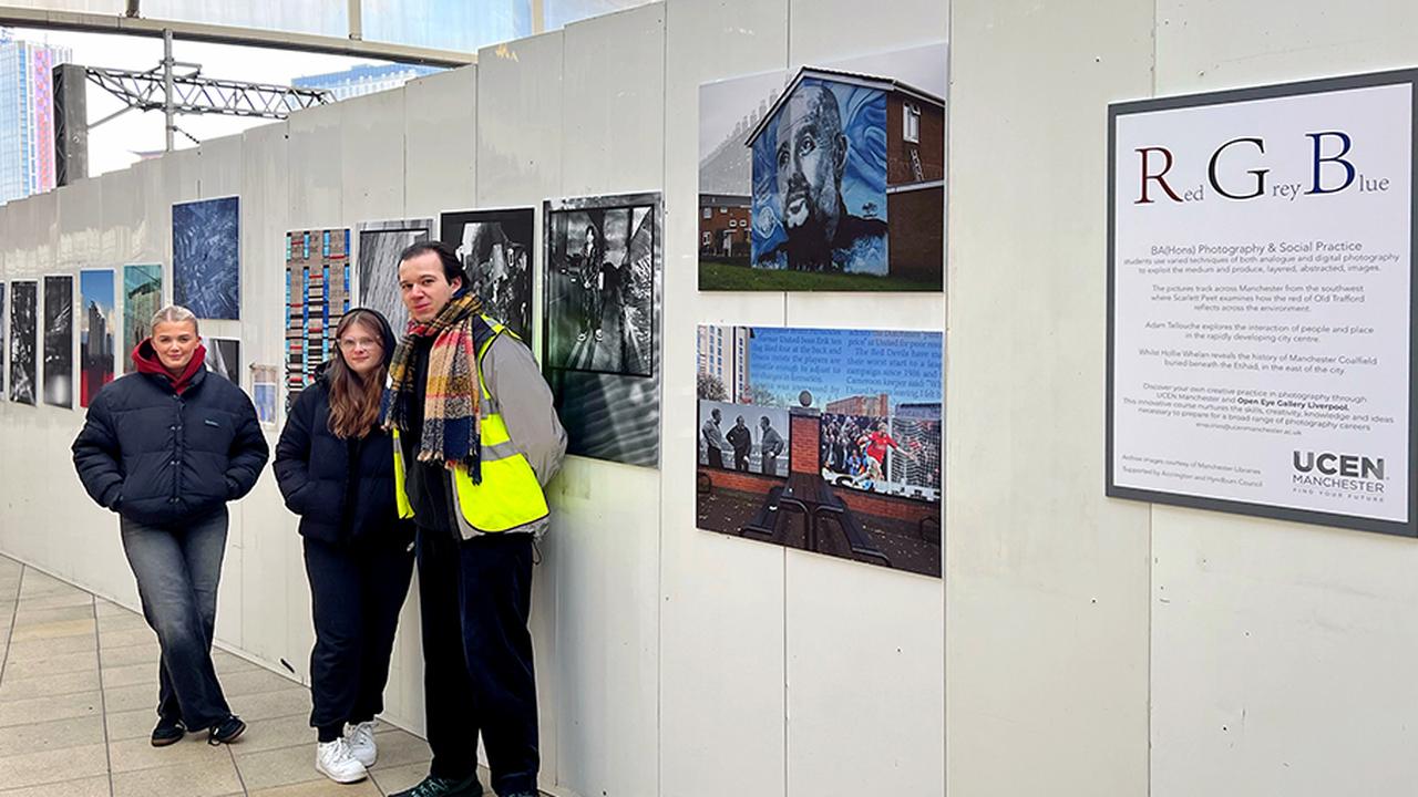 Three UCEN Manchester Photography students stand beside their work on display at Manchester Victoria station.