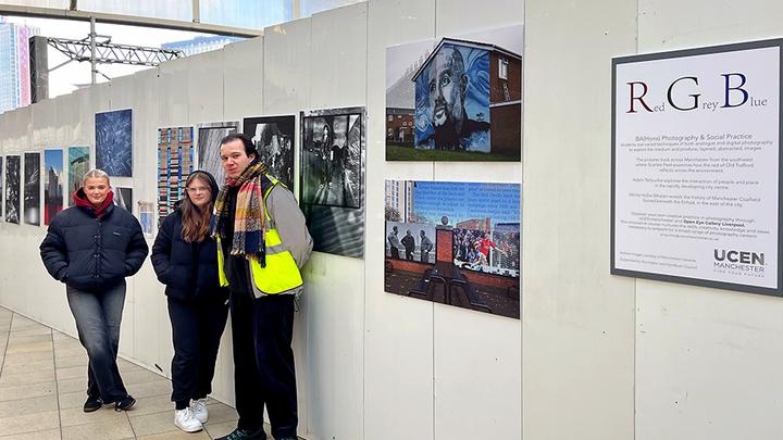 Three UCEN Manchester Photography students stand beside their work on display at Manchester Victoria station.