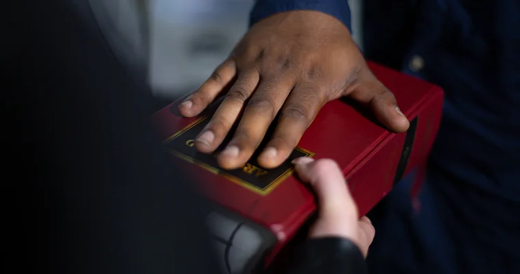 Close-up of one person placing a hand on a red bible while another person holds it, suggesting an oath-taking.