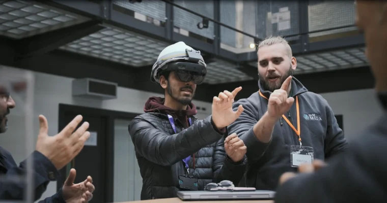 Person wearing a mixed reality headset interacts with virtual content while being guided by an instructor in a technology learning environment.