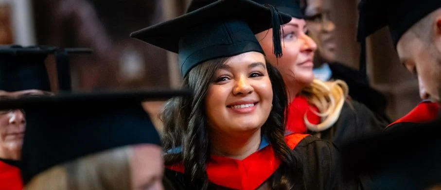 Graduate in cap and gown seated among fellow graduates during a graduation ceremony.