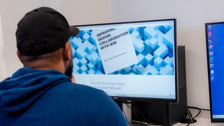 Person seated at a computer viewing an article titled “Improving Design Collaboration with BIM” on a large monitor.