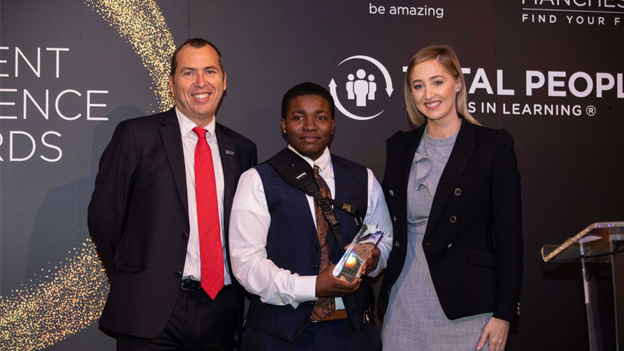 Three people stood for a photo with one holding an award