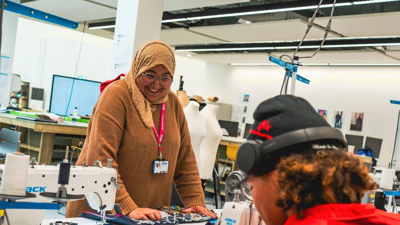 A smiling UCEN Manchester student working with textiles at a sewing machine workshop station.