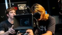Student operating professional broadcast camera equipment in a media production studio while another student assists.