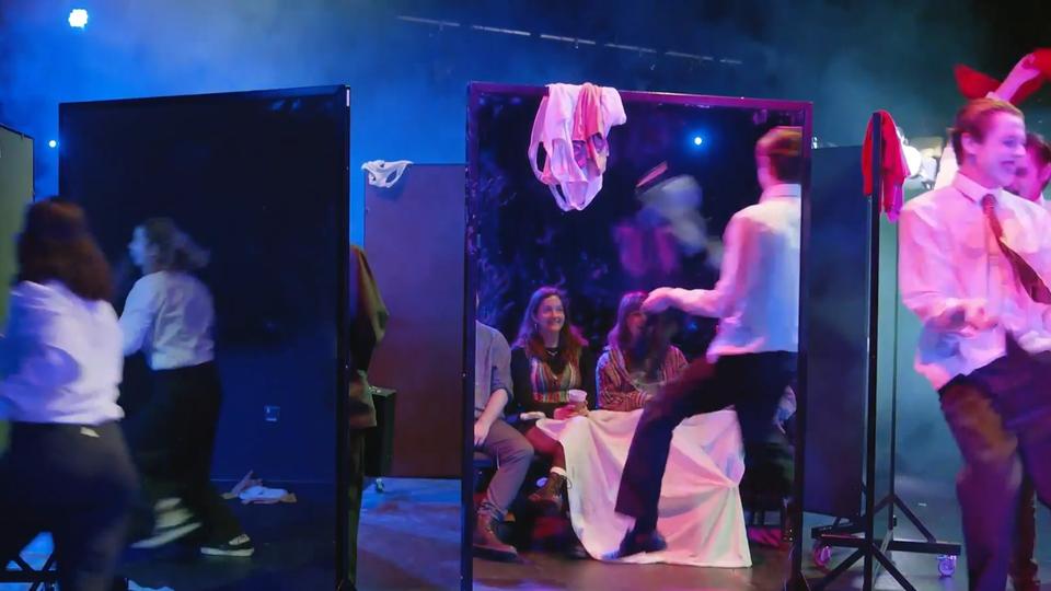 Theatre and performance students in the middle of a production, running around a blue stage with mirrors