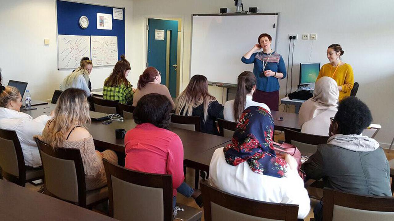 A class of students listening to two teachers stood at the front of the room