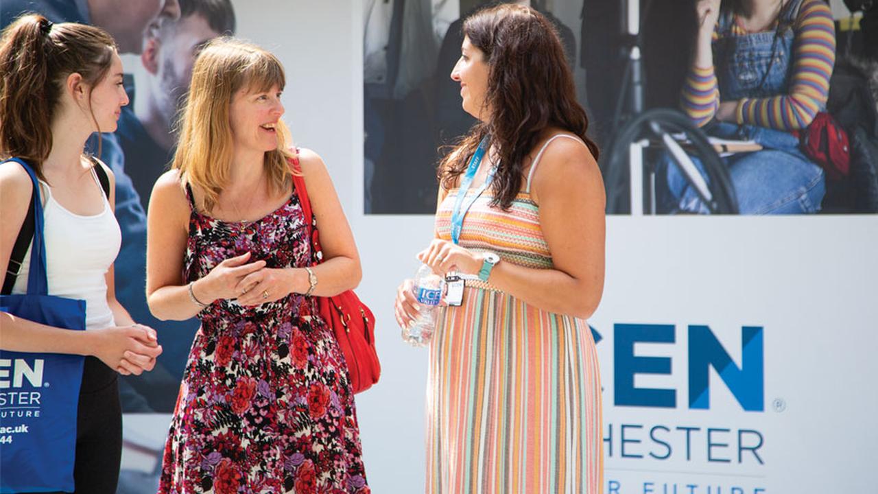 Three woman stood talking in front of a UCEN sign