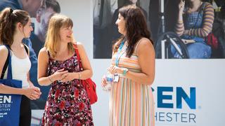 Three woman stood talking in front of a UCEN sign