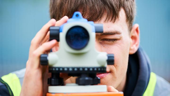 A construction student looks through an automatic level, straight down the camera.