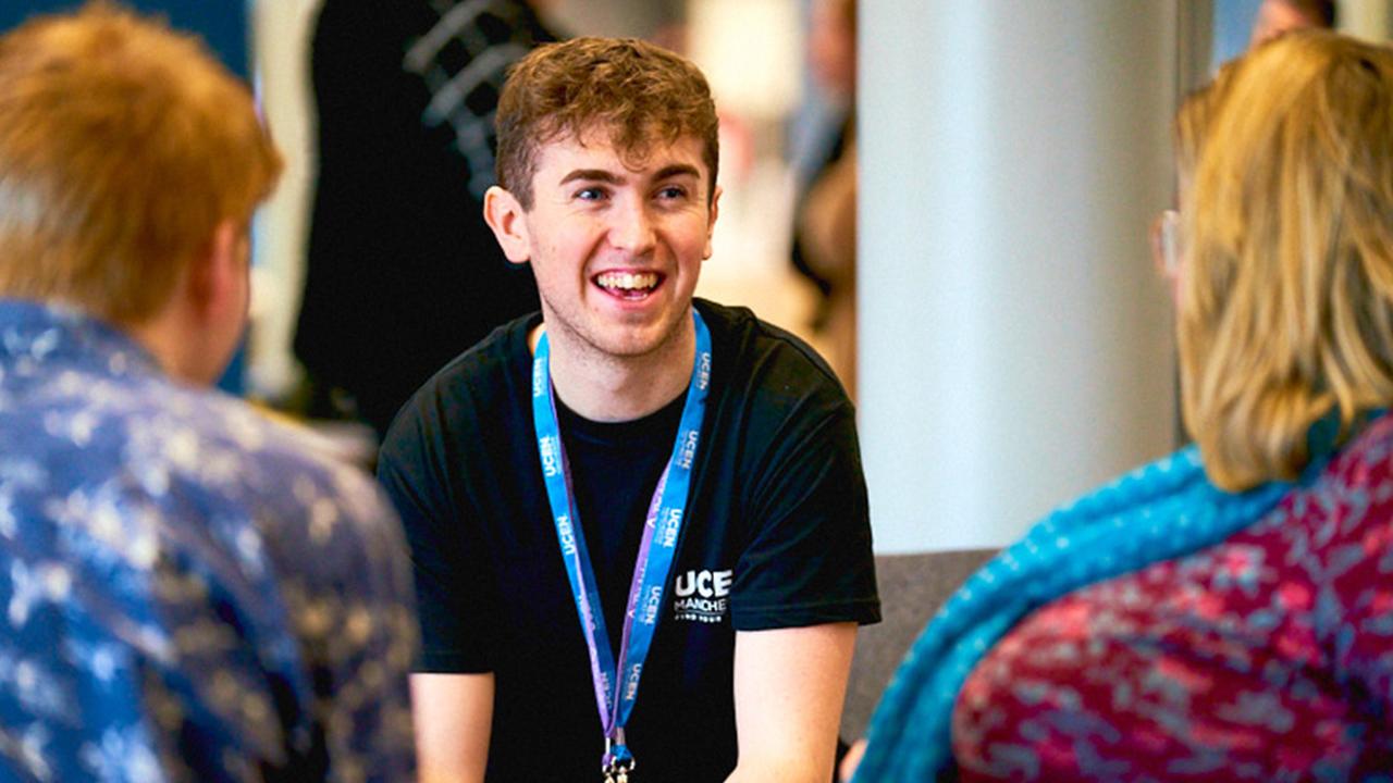 Photograph of a current UCEN Manchester student talking to two guests at an open event.