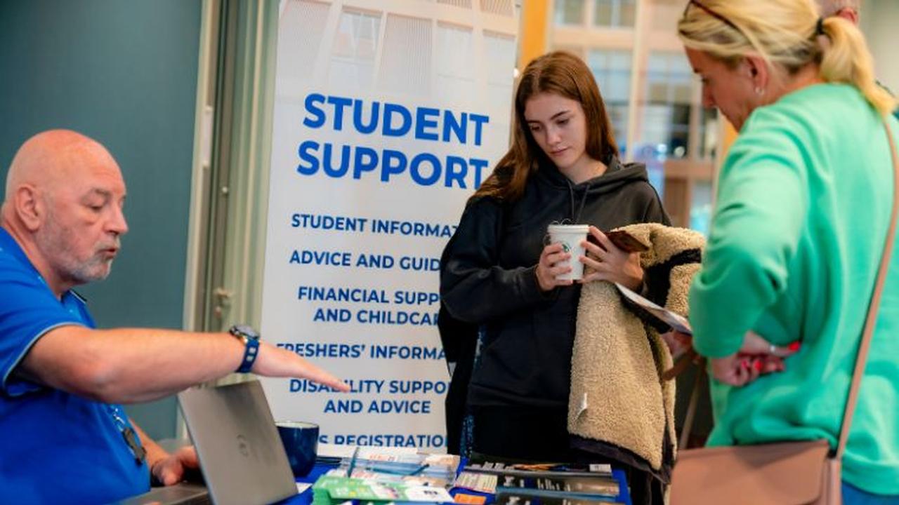 Student speaking with support staff at a student information stand displaying guidance on financial support, childcare and student services at UCEN Manchester.
