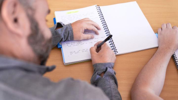 Over-the-shoulder view of someone writing in a notebook