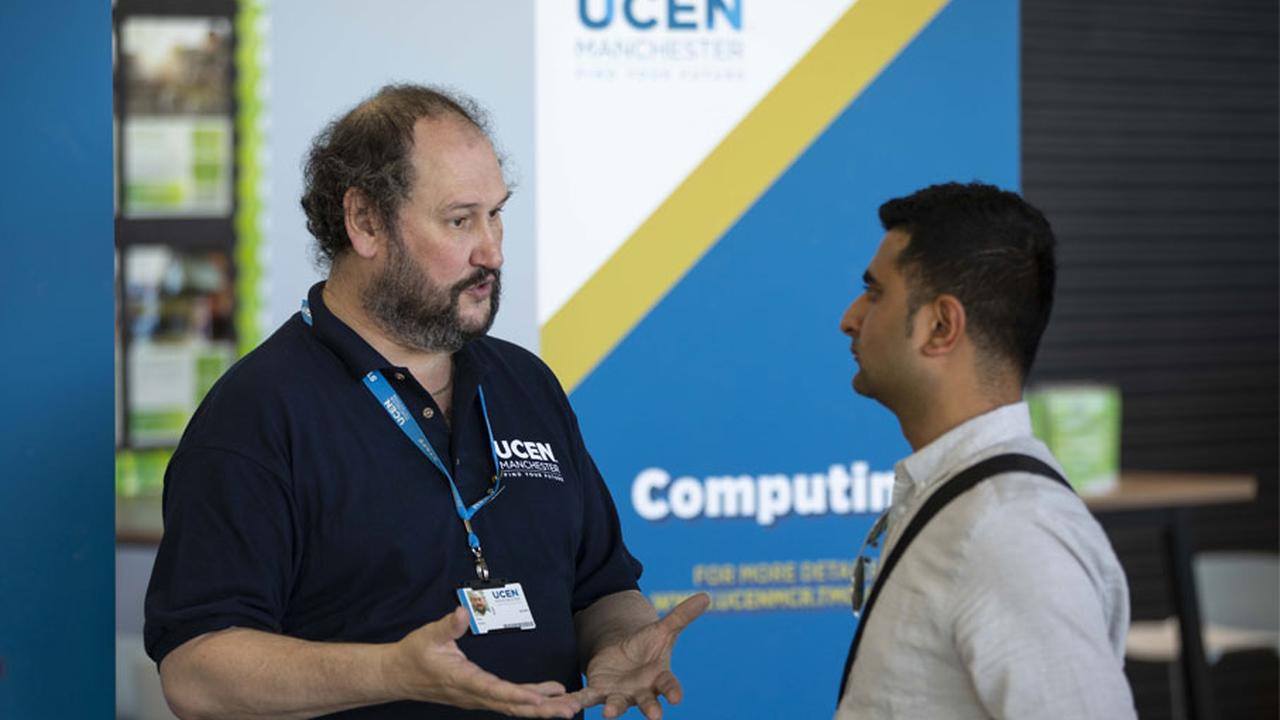 Two men stood talking in front of a UCEN Manchester banner