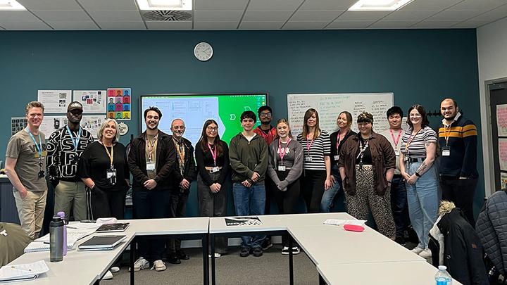 Graphic Design students standing with UNISON staff in a classroom after pitching to them.