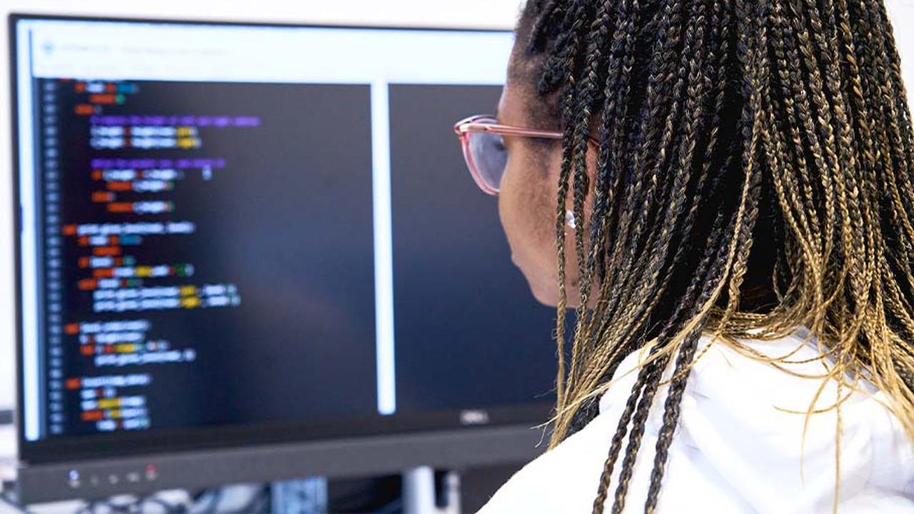 A woman is looking at a black computer screen with rows of code on at The Manchester College.