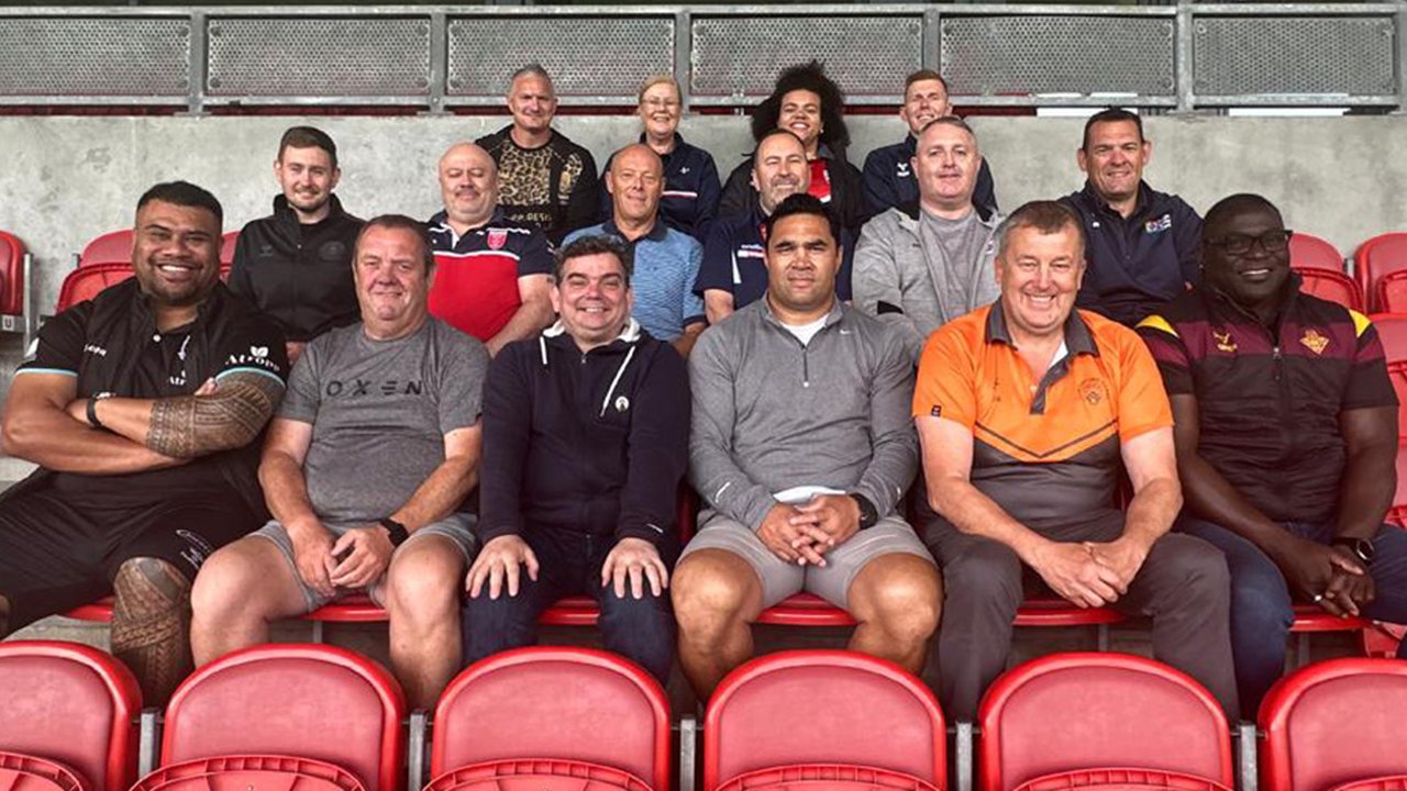 Photograph of a group of Player Welfare Managers sat in the stand at a rugby league stadium.