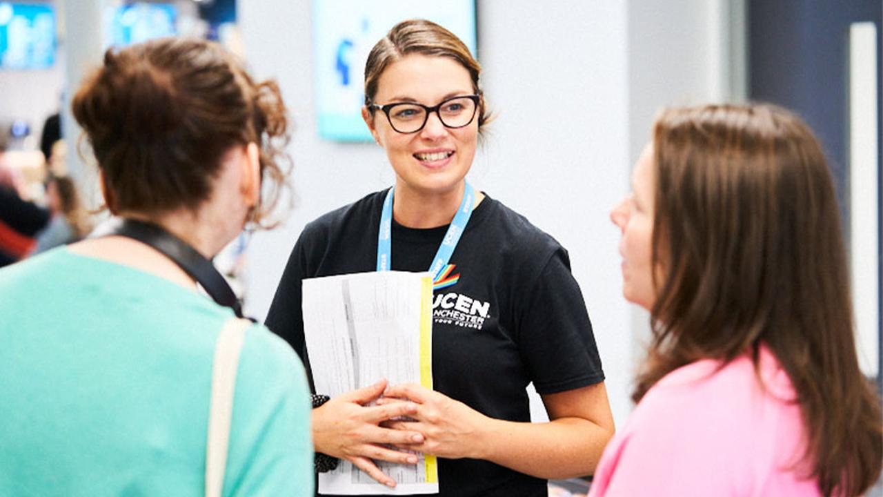 A colleague in a UCEN Manchester t-shirt chats to two visitors at an Open Event.