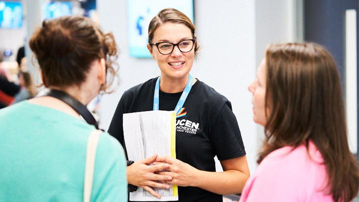 A colleague in a UCEN Manchester t-shirt chats to two visitors at an Open Event.