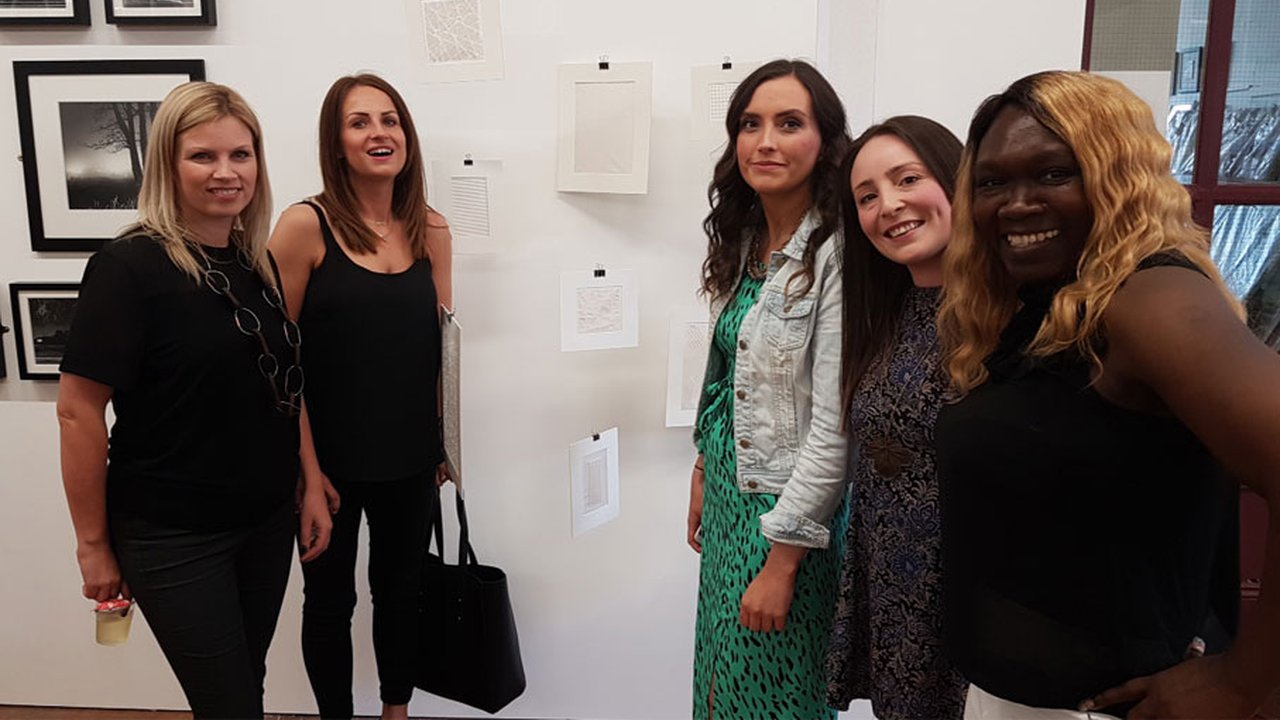 A group of woman stood posing in front of an art exhibit