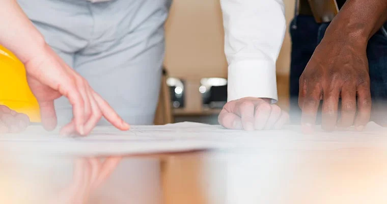 Several people review and point to documents spread across a table during a collaborative planning session.
