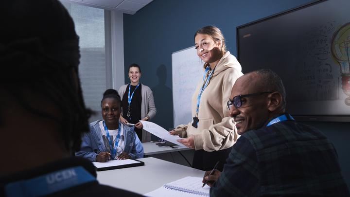 Business student stood presenting in front of her class and tutor